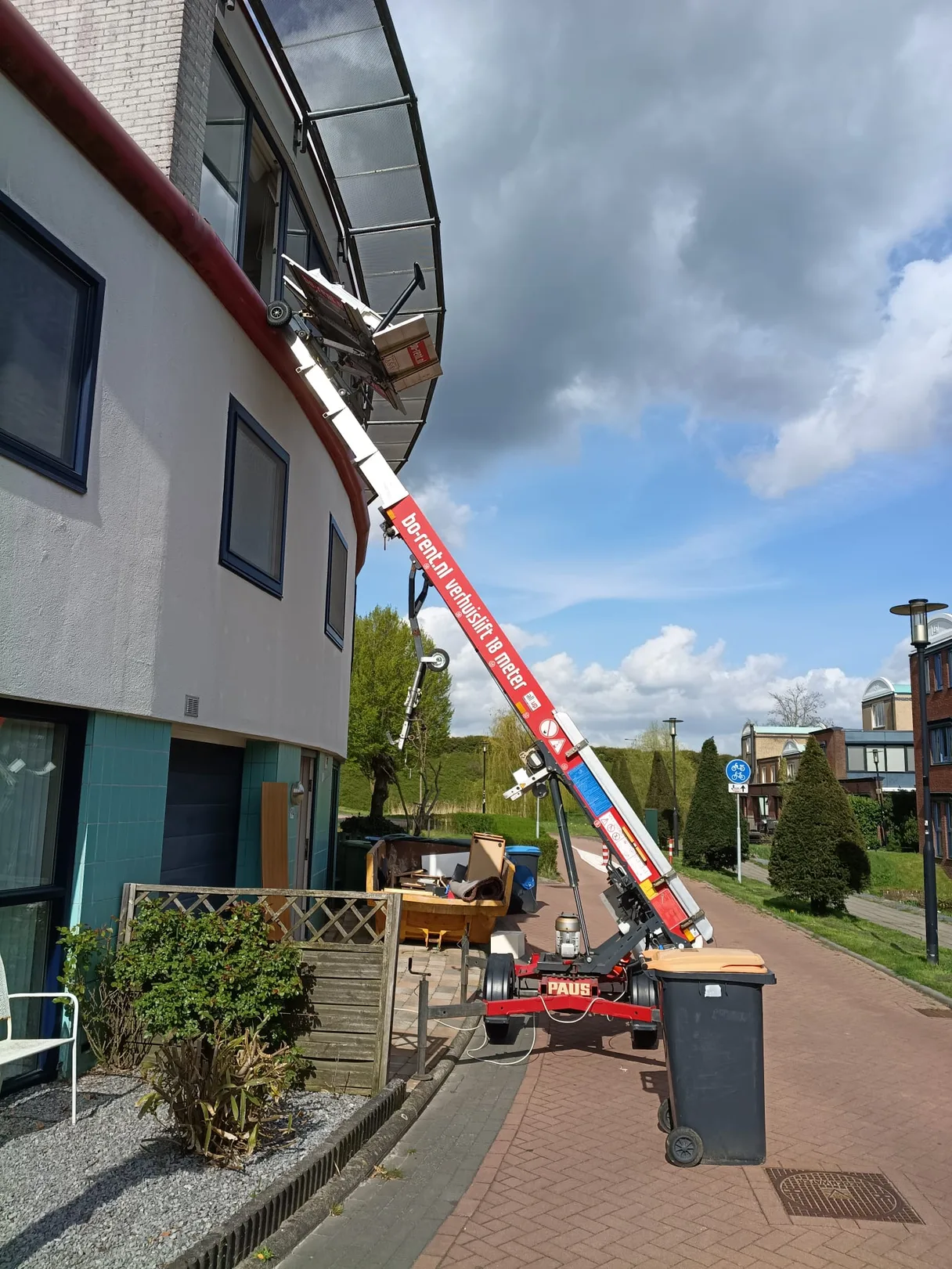 Verhuislift van 18 meter tegen een appartement, met meubels op straat klaar voor afvoer tijdens een ontruiming