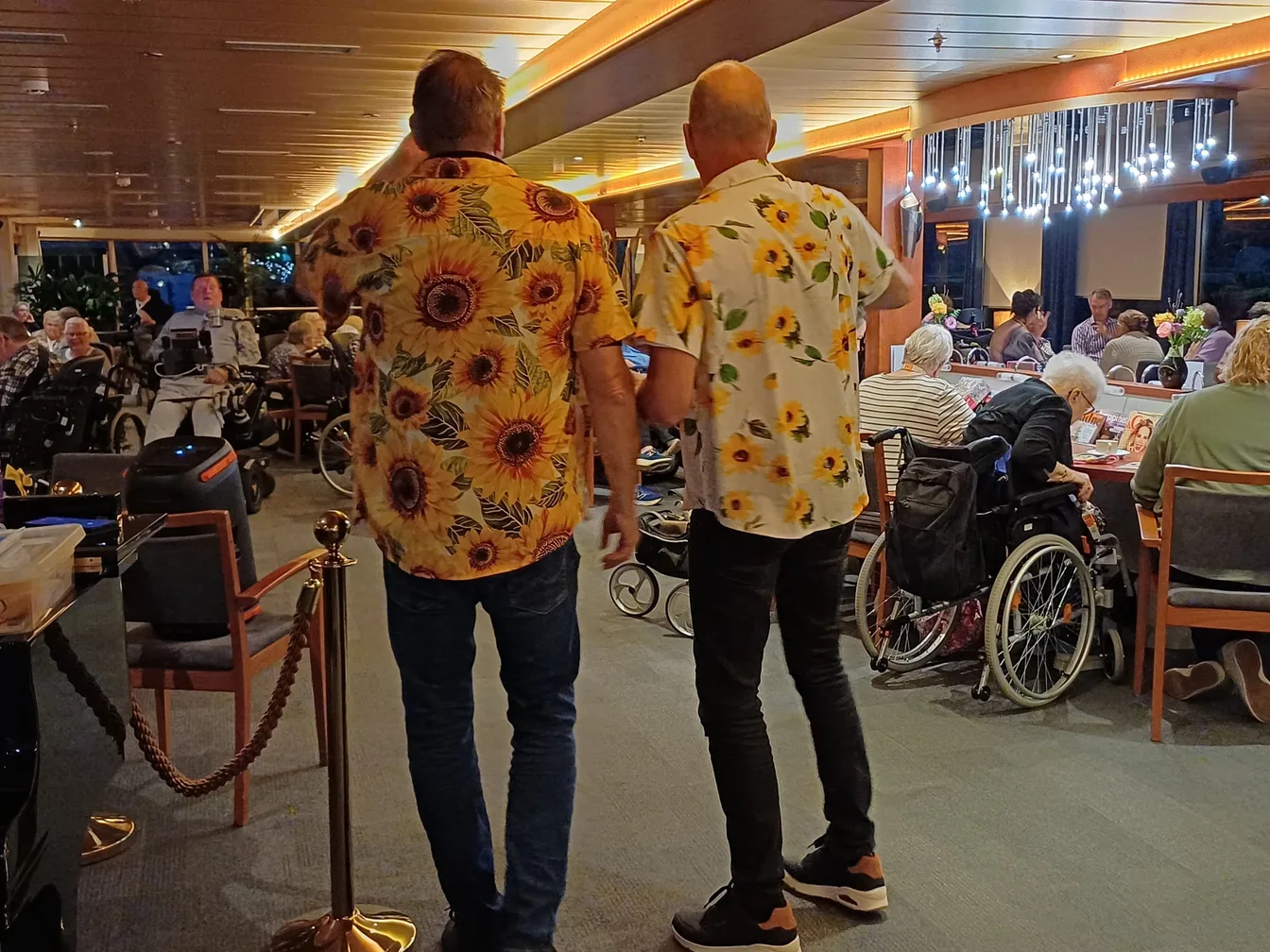 René in zonnebloemshirt tussen de gasten in de salon van het Zonnebloem-schip
